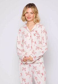 Witte pyjama set met rode strikpatronen, lange mouwen en contrasterende rode afwerking. Zachte stof met knoopsluiting bovenkant en bijpassende broek.