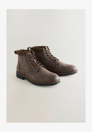 Bruine leren enkellaarsjes met een gestructureerde afwerking, ronde neus en donkere rubberen zool. Voorzien van bruine veters en een gebreide boorden aan de bovenkant.
