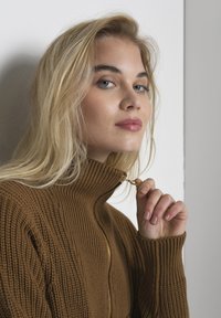 Pull en tricot brun avec un col montant et un détail de fermeture éclair doré. Il présente une texture côtelée et des manches longues. Tissu doux avec une silhouette ajustée.