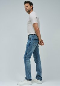 Vaqueros de mezclilla azul claro con un ajuste relajado, costuras visibles y una cintura con trabillas. Llevados con una camiseta beige y zapatillas blancas.