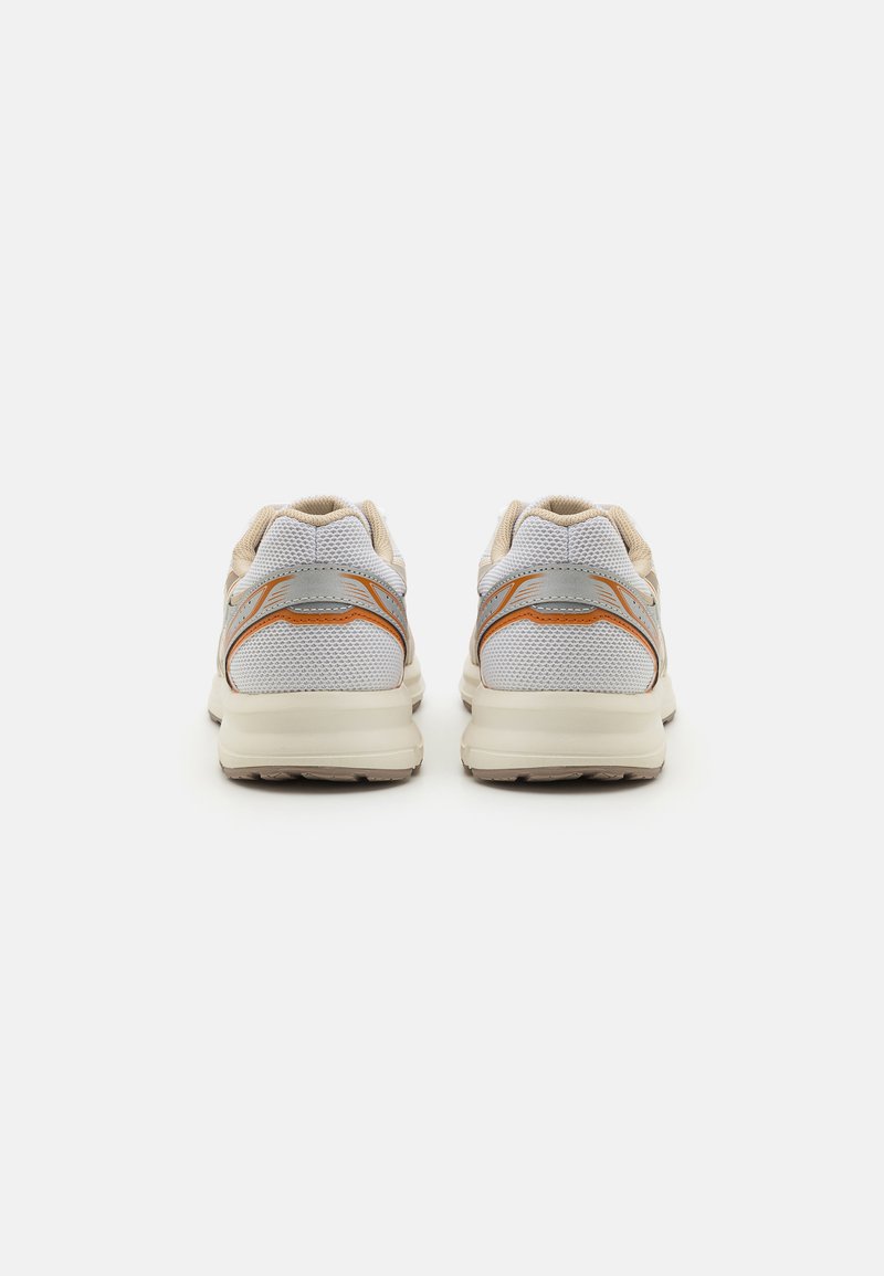 Weiße Sportschuhe mit einem Netzobermaterial, beigefarbenen Akzenten und grauen Details, ausgestattet mit einer strukturierten Sohle und einem gepolsterten Kragen für zusätzlichen Komfort.