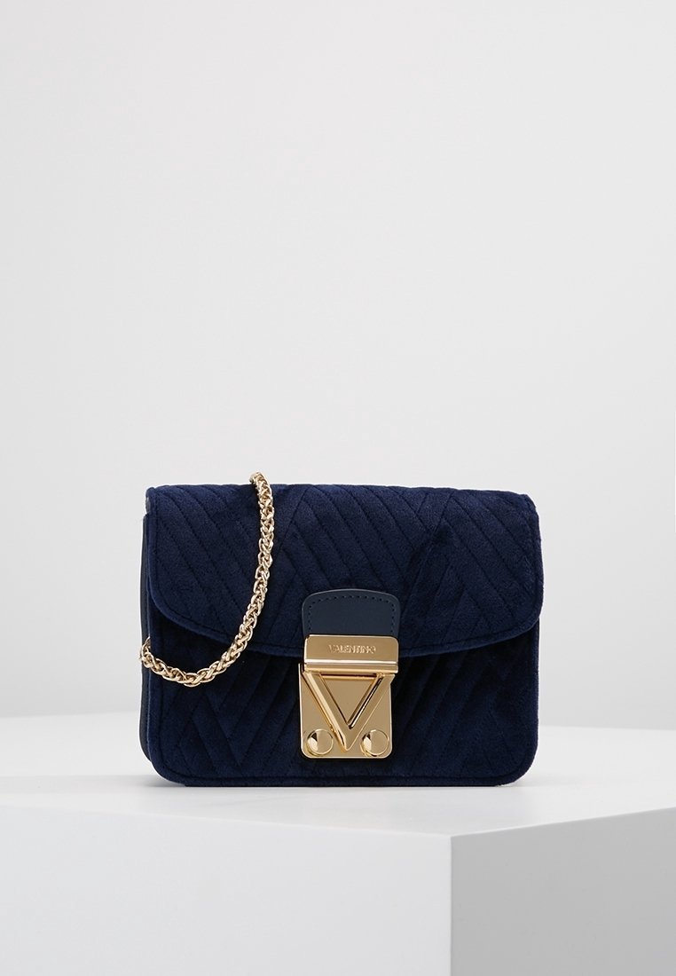 Navy-blaues gestepptes Wildleder-Handtasche mit goldenen Beschlägen, ausgestattet mit einer Kettenriemen und einem auffälligen Verschluss, der ein V-Logo-Detail auf der Vorderseite zeigt.