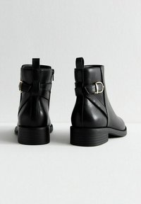 Botas de tobillo de cuero negro con un acabado suave, punta redonda, tacón bajo apilado y detalle decorativo de hebilla en la parte posterior.