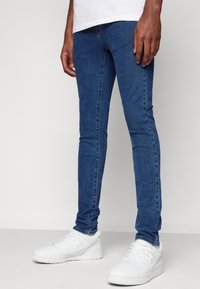 Modré džíny skinny z denimu s hladkou texturou, přilnavým střihem a mírně odřenými místy; doplněné bílými teniskami.