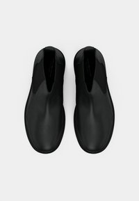 Sapatos pretos slip-on com parte superior em pele lisa, inserções laterais elásticas, bico arredondado e design minimalista. Sem ferragens ou detalhes visíveis.