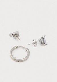 Cercel din argint în formă de cerc, alături de două cercei tip stift, unul dreptunghiular cu o piatră clară, iar celălalt cu un design simplu de bară, toate având finisaje metalice netede.