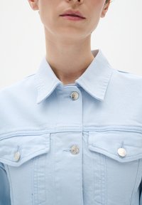 Gai zils džinsisjakas ar apkakli, sudraba pogu akcentiem un krūšu kabatām. Audumam ir gluda tekstūra ar redzamām šuvēm.