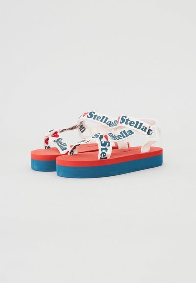 Sandalias de plataforma con una suela superior roja, suela inferior azul y correas blancas que presentan el texto "Yo amo a Stella". Diseño plano, estilo casual.