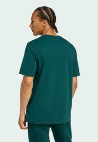 Zelené bavlnené tričko, krátke rukávy, okrúhly výstrih, voľný strih, hladká textúra. Model je zobrazený zozadu, v kombinácii s nohavicami v rovnakom štýle.