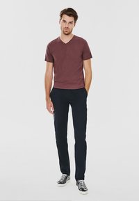 Ciemnoczerwony t-shirt z dekoltem w serek, dopasowane granatowe spodnie i czarno-białe sneakersy. Gładki materiał i minimalistyczny design.