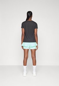 T-shirt preta de manga curta combinada com calções verde menta, apresentando um design em camadas. O modelo está a usar ténis brancos e meias.