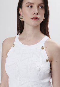 Top tank in maglia bianca con un motivo texturizzato e dettagli in bottone dorato sulle spalline. Tessuto liscio e design aderente.