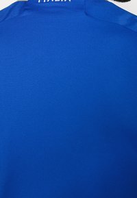 Niebieska koszulka sportowa z teksturowanej tkaniny. Posiada okrągły dekolt i napis "ITALIA" na plecach. Gładki i lekki materiał.