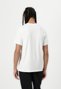 Bílý bavlněný tričko s kulatým výstřihem, krátkými rukávy a rovým lemem, který má hladkou texturu a žádné viditelné logo nebo vzory.