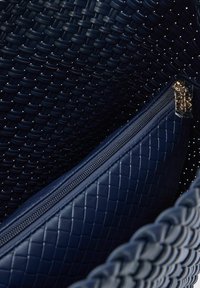 Geweven marineblauwe handtas met een textuurinterieur en een gestikte ritszak. Voorzien van gouden hardware op de rits.