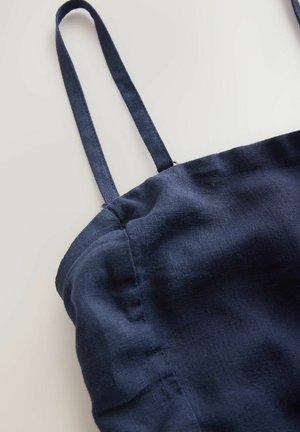 Tmavě námořnicky modrá lněná látka s tenkými řemínky. Textura působí mírně pomačkaně a ukazuje měkký, lehký design.