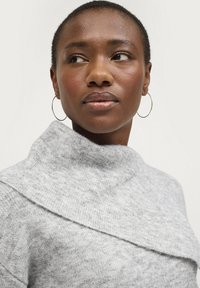 Grau gestrickter Pullover mit hohem Kragen und mehrschichtigem Design. Verfügt über eine weiche Textur und eine enganliegende Silhouette. Schlichte, runde Creolen.