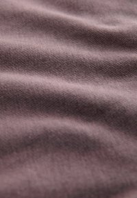 Teksturowana tkanina w kolorze mauve, z delikatnymi falami i gładkim wzorem na powierzchni, z subtelnym połyskiem odbijającym światło.