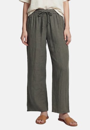 Pantaloni larghi verde oliva con elastico in vita e coulisse, indossati con sandali scamosciati color cammello e top beige chiaro.