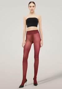 Rote undurchsichtige Strumpfhose mit halbtransparentem Effekt, ausgestattet mit einem hohen Bund und glatter Textur. Getragen mit einem schwarzen trägerlosen Oberteil und High Heels.