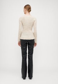 Bežani pleteni pulover s prilagođenim dizajnom, dugim rukavima i peplum rubom, uparen sa crnim sjajnim širokim hlačama. Čist, minimalistički stil.
