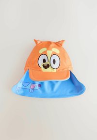 Gorra naranja con cara de perro de dibujos animados, con orejas caídas y ojos grandes. El visor azul incluye una imagen impresa de un perro. Material suave y ligero.