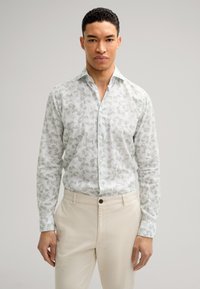 Hellgrünes, gemustertes Hemd mit Kragen, langen Ärmeln und weißem Hintergrund; kombiniert mit cremefarbenen Hosen.