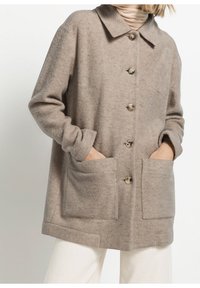 Cappotto in misto lana beige con colletto, bottoni frontali e due ampie tasche a toppa. Presenta un tessuto morbido e strutturato.