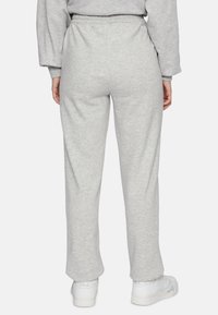 Lichtgrijze sweatpants met een elastische tailleband, recht model en een zachte textuur. Gecombineerd met witte schoenen voor contrast.