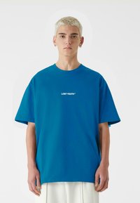 Blå bomulds T-shirt med korte ærmer, der har et hvidt "LOST YOUTH" logo på brystet. Afslappet pasform og rund halsudskæring.