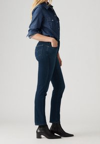 Blauwe denim shirt met knoopsluiting, gecombineerd met donkerblauwe slim-fit jeans en zwarte enkellaarsjes met blokhak en spitse neus.