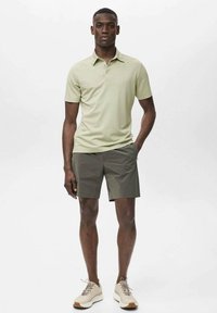 Ljusgrön polo med krage, kombinerad med mörkgröna shorts. Modellen bär beiga sneakers med bruna accenter. Enkel, sportig design.