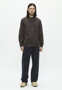 Bruine sweatshirt met ribgebreide manchetten en een ronde hals, gecombineerd met loszittende marineblauwe broek en tan instap schoenen. Geen zichtbare patronen.