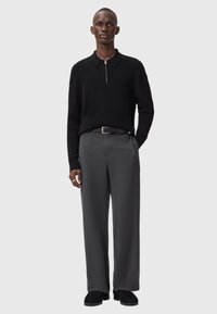 Black knit polo sweater with a zippered collar, paired with gray wide-leg trousers and black shoes, featuring a slim belt and textured fabric.