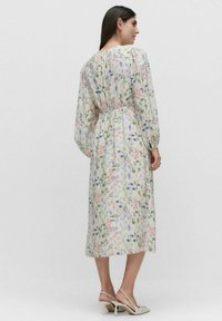 Kukallinen midi-mekko pitkillä hihoilla, kootulla vyötäröllä ja kevyellä, puolikuultavalla kankaalla, jossa on monivärisiä kukkakuoseja vaalealla taustalla.