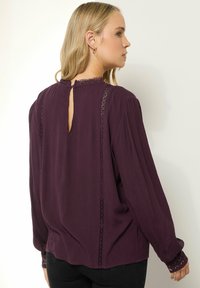 Blusa a maniche lunghe in prugna con tessuto testurizzato, schiena a chiave, dettagli in pizzo lungo i lati e polsini elasticizzati con un motivo.