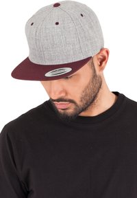 Szürke snapback sapka vörös szegéllyel és szemlyukakkal; texturált anyagból készült; kerek forma; lapos csúcs; állítható pánt hátul.