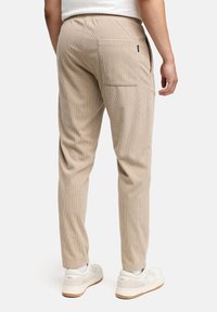 Pantaloni di velluto a coste beige con vestibilità dritta, dotati di una tasca posteriore e una cintura elastica, abbinati a sneakers bianche per un effetto a contrasto.