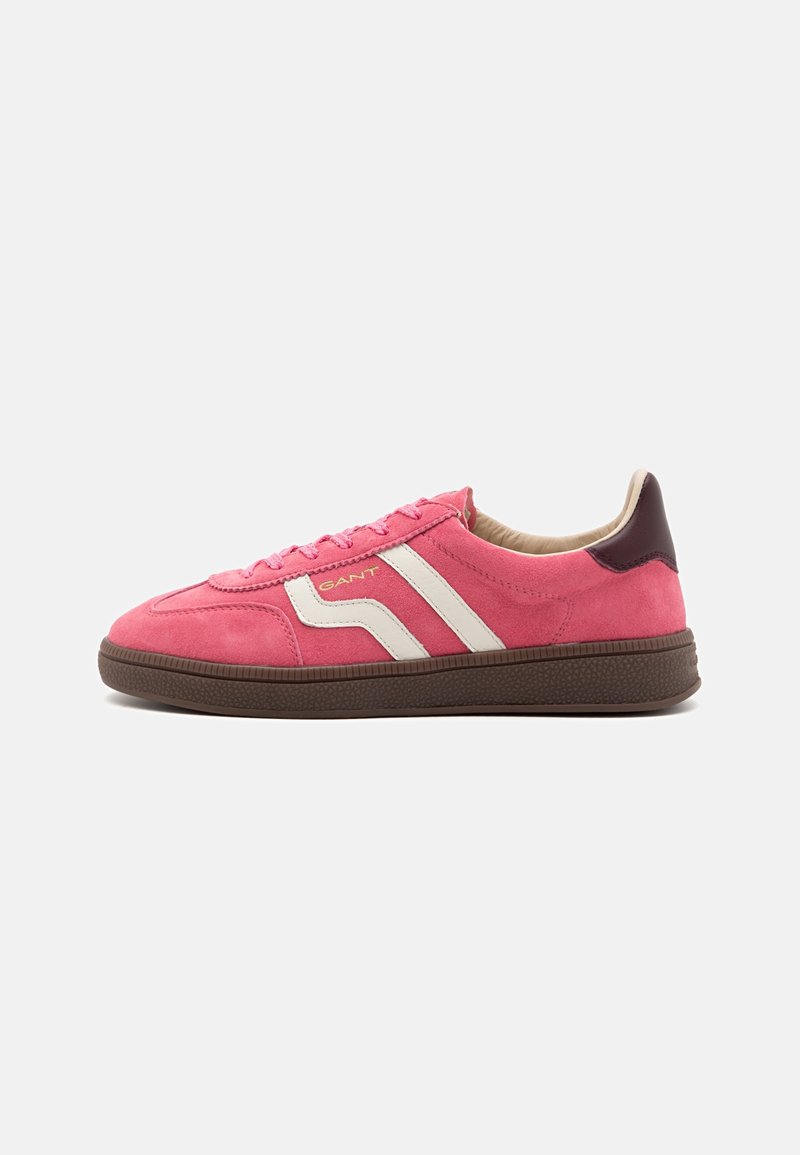 Baskets en daim rose avec des bandes blanches sur les côtés, semelle marron et patch talon marron foncé, montrant la vue latérale gauche de la chaussure sur fond blanc.