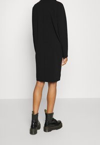 Czarna sukienka z długim rękawem o prostym kroju, z designem slip. Połączona z błyszczącymi czarnymi butami wojskowymi z żółtymi akcentami.