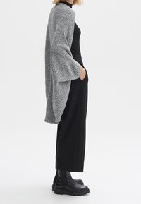 Szary dziany kardigan z szerokimi rękawami, w połączeniu z czarnym topem i luźnymi czarnymi spodniami. Grube czarne botki z teksturowaną podeszwą.