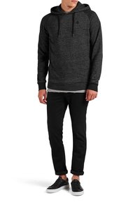 Svart huvtröja med texturerad yta, raglanärmar och justerbar dragsko. Kombinerad med smala svarta byxor och sneakers.