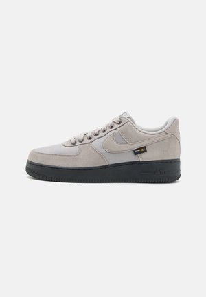 Lichtgrijze Nike Air Force 1 sneaker met bovenwerk van suède en mesh, zwarte zool en een klein Cordura stoffen label aan de zijkant.