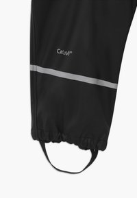 Black waterproof pants with a cinched ankle, featuring a reflective silver stripe and a branded logo, made from smooth, durable material.