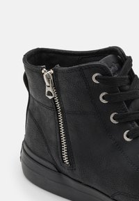 Melni potītes zābaki, izgatavoti no teksturētas mākslīgās ādas, ar metāla rāvējslēdzēju un acu caurumiem, ar platu gumijas zoli un auklām.