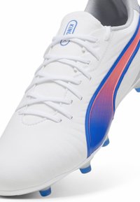 Scarpette da calcio bianche con tomaia testurizzata, caratterizzate da accenti in gradiente blu e rosa, sei lacci bianchi e tacchetti blu sulla suola.