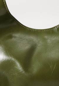 Green, textured faux leather fabric with a glossy finish; features a rounded neckline and stitching along the edge.