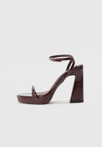 Burgundy patent leather heeled sandals with a thick square heel, thin ankle strap, and minimalist toe loop design. Smooth glossy finish.