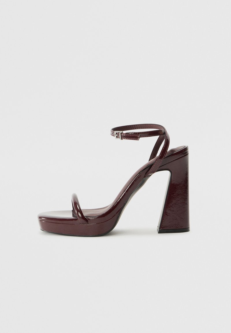 Burgundy patent leather heeled sandals with a thick square heel, thin ankle strap, and minimalist toe loop design. Smooth glossy finish.