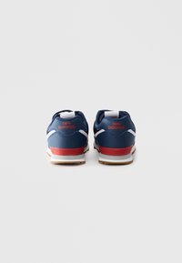 Une paire de baskets New Balance bleu marine avec des accents rouges et blancs, vue de dos sur un fond blanc uni.